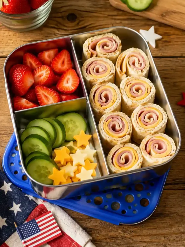 Stainless steel kids’ bento box with ham and cheese pinwheels, strawberries, cucumber slices, and star-shaped cheese.