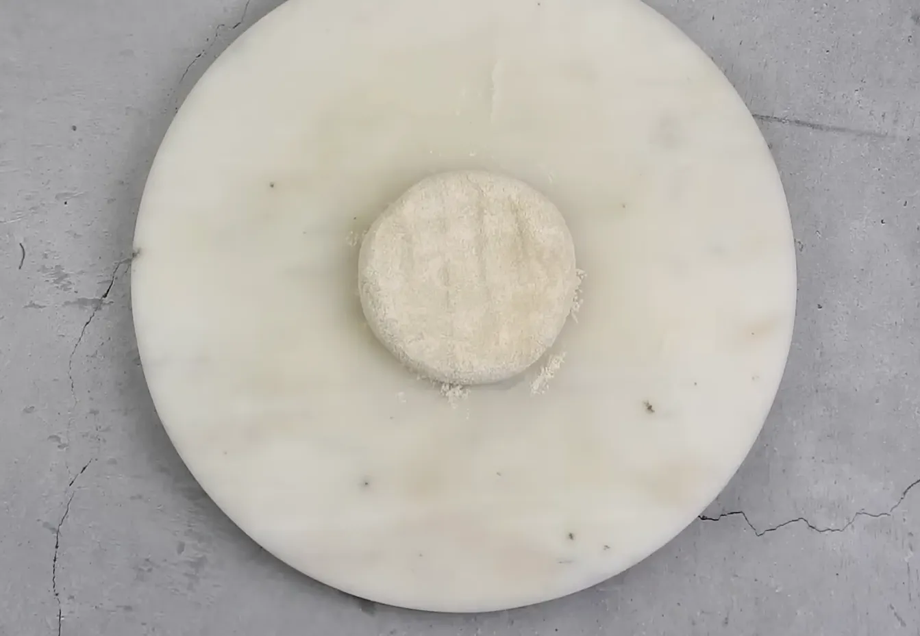 Round dough ball dusted with dry flour on a wooden rolling board