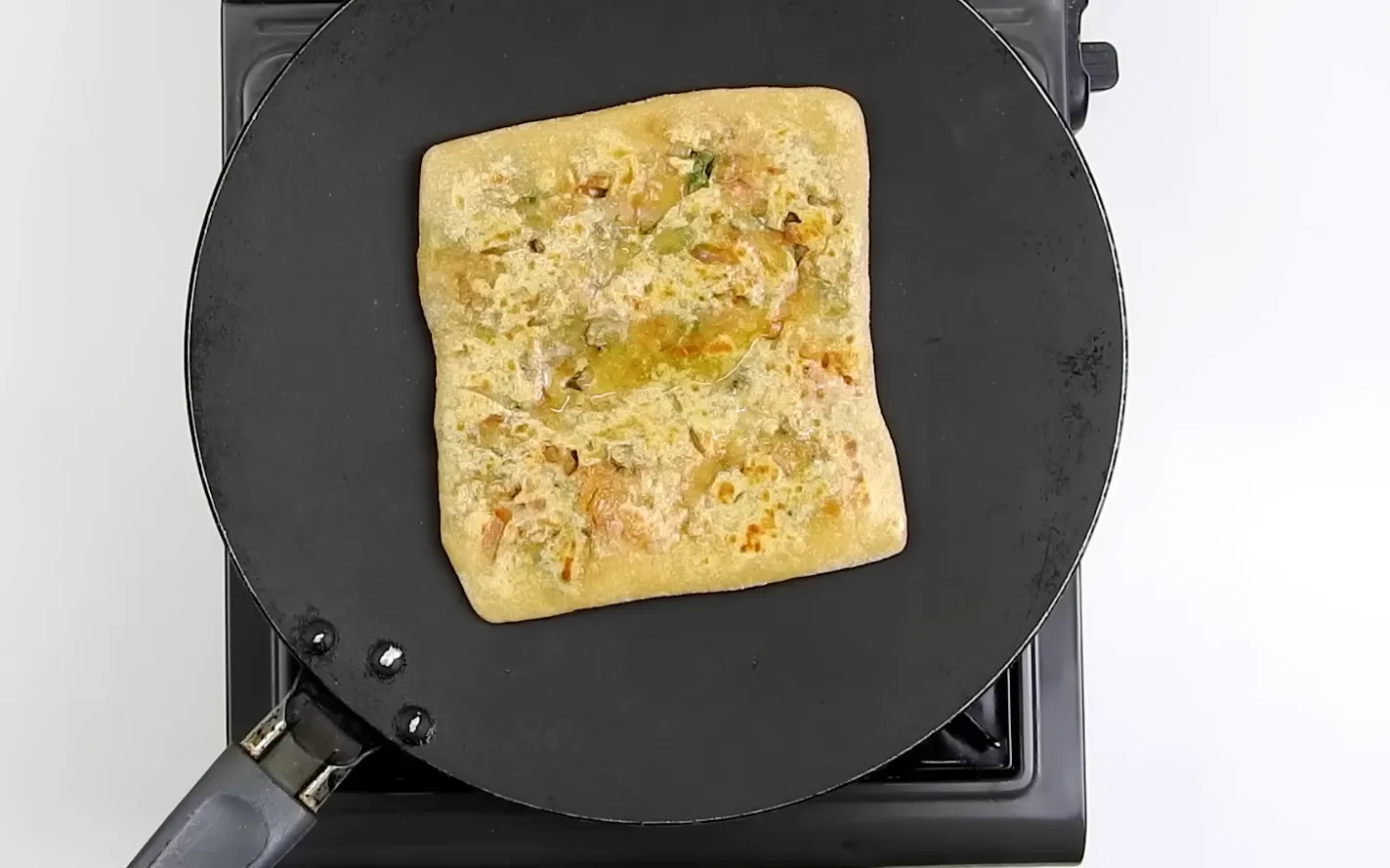 Golden crispy square onion paratha frying on a hot tawa with oil