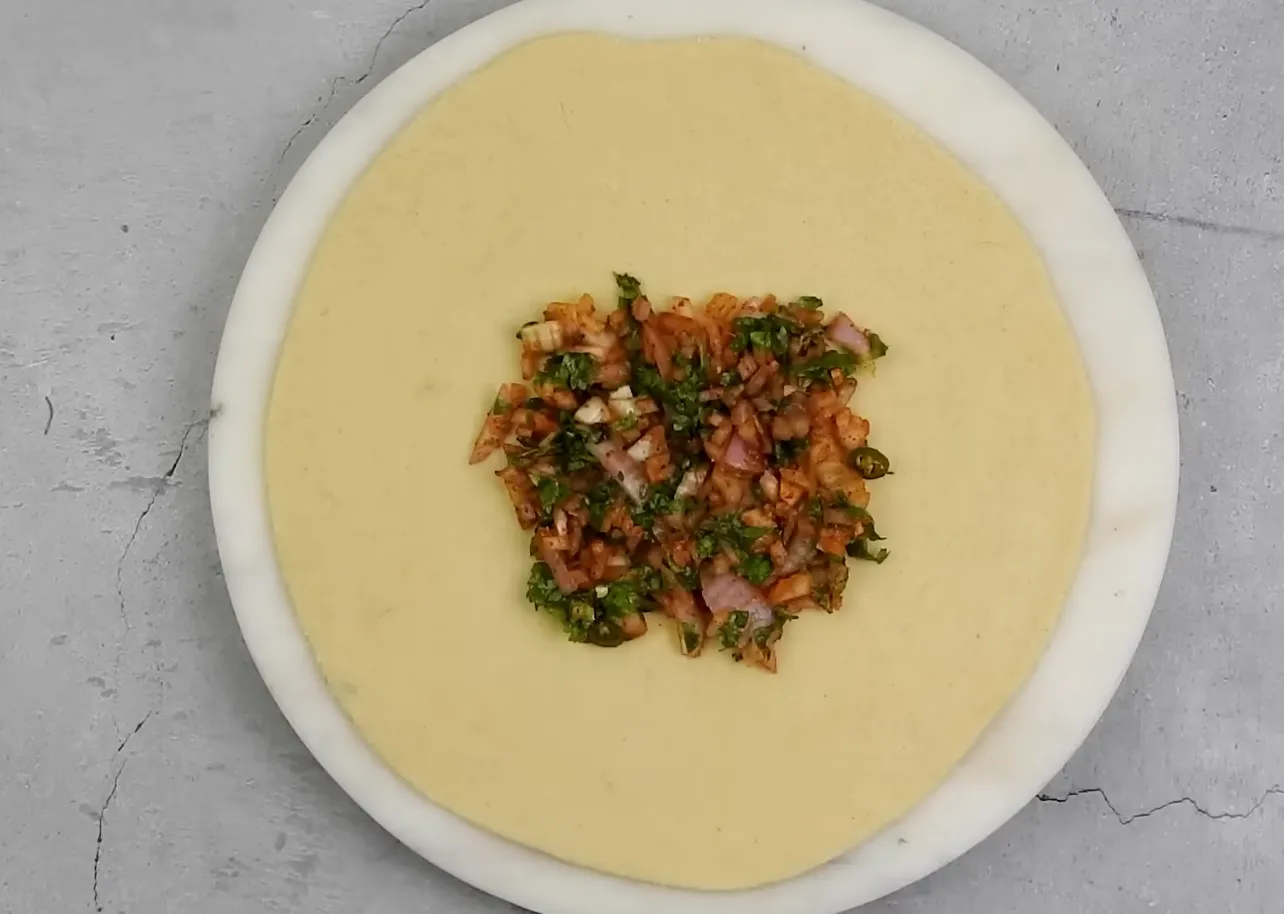 Flat rolled wheat dough disc topped with square onion filling in the center
